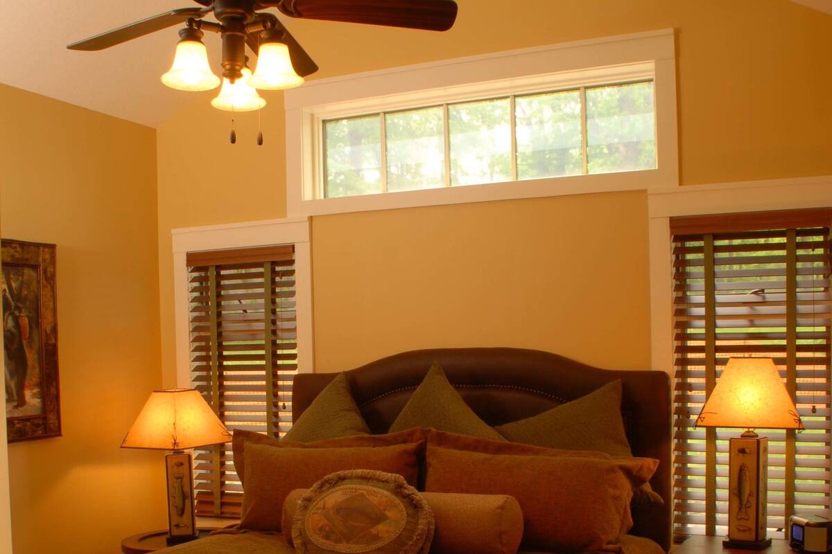 A bedroom with a bed, two bedside lamps, a ceiling fan, and a window with blinds.