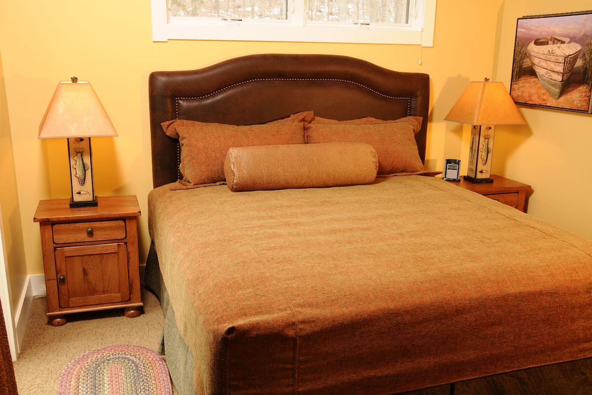 A neatly made bed with a brown headboard, two bedside tables with lamps, and a framed picture on the wall.