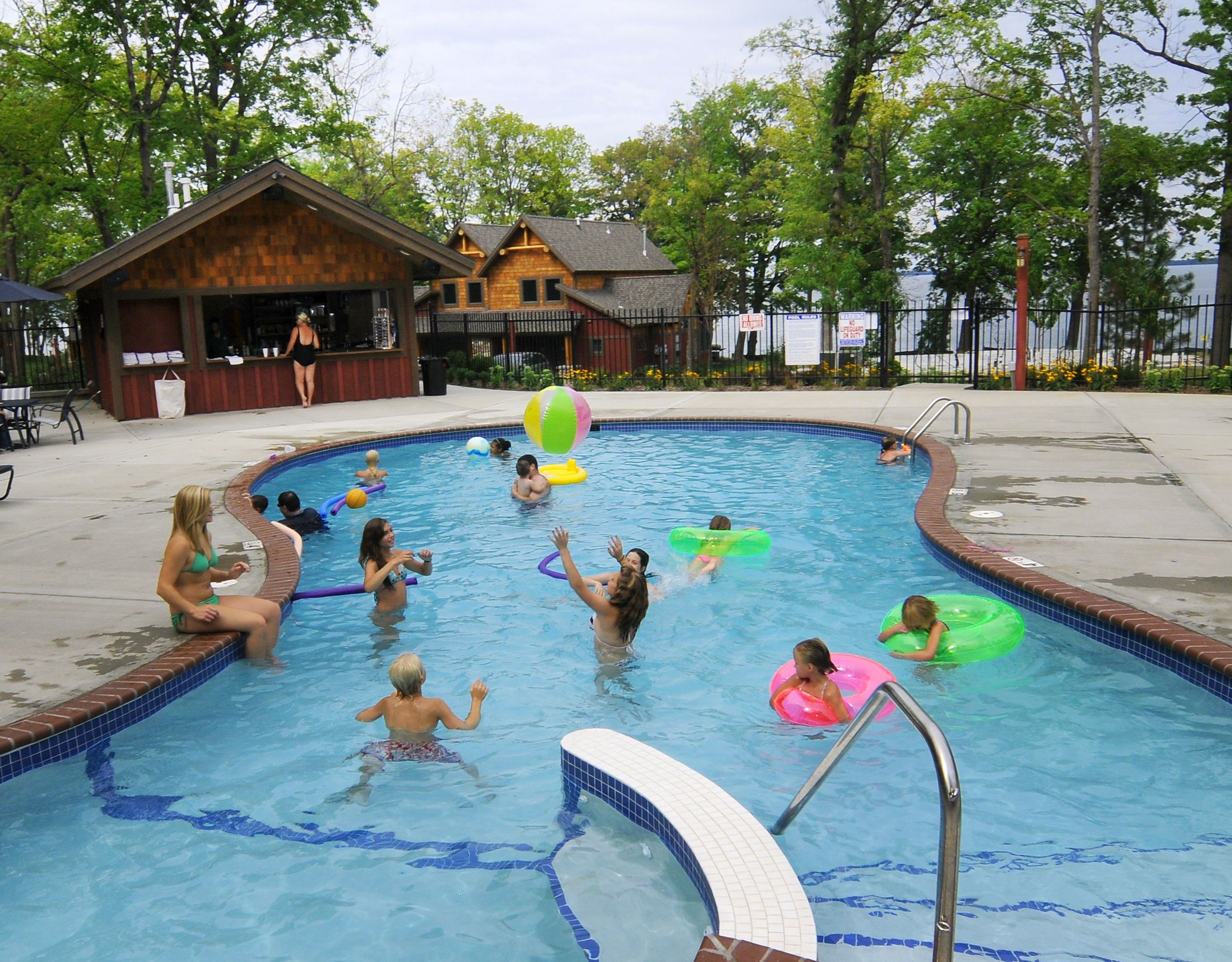 A swimming pool with people enjoying the water, surrounded by a wooden building and trees.