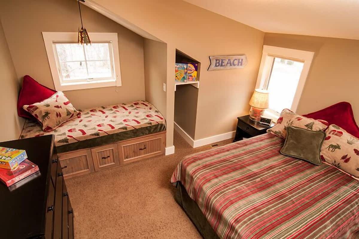 A bedroom with two beds, a window, a shelf with toys, and a 'BEACH' sign on the wall.