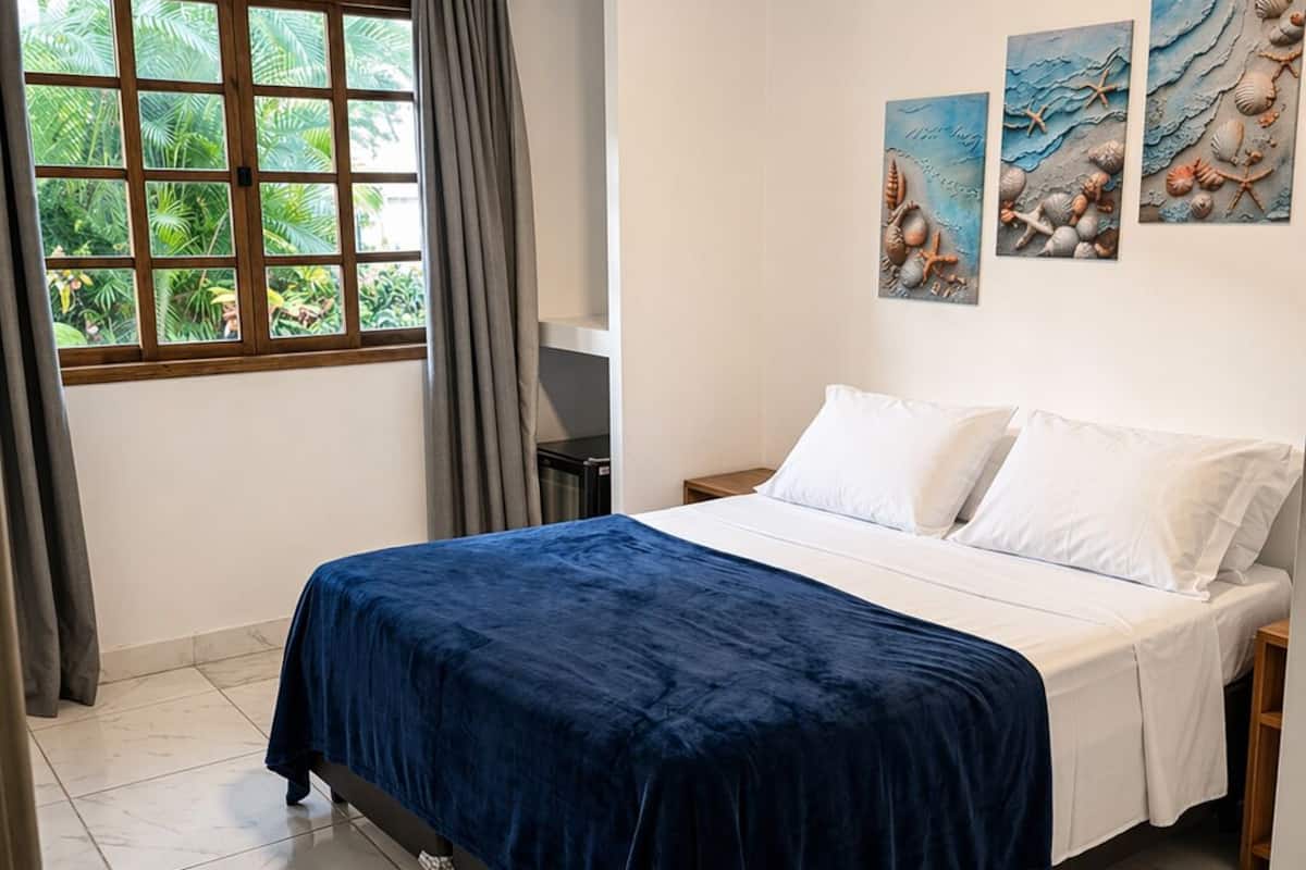 Une chambre à coucher avec un lit, une fenêtre avec des rideaux et des œuvres d’art murales.