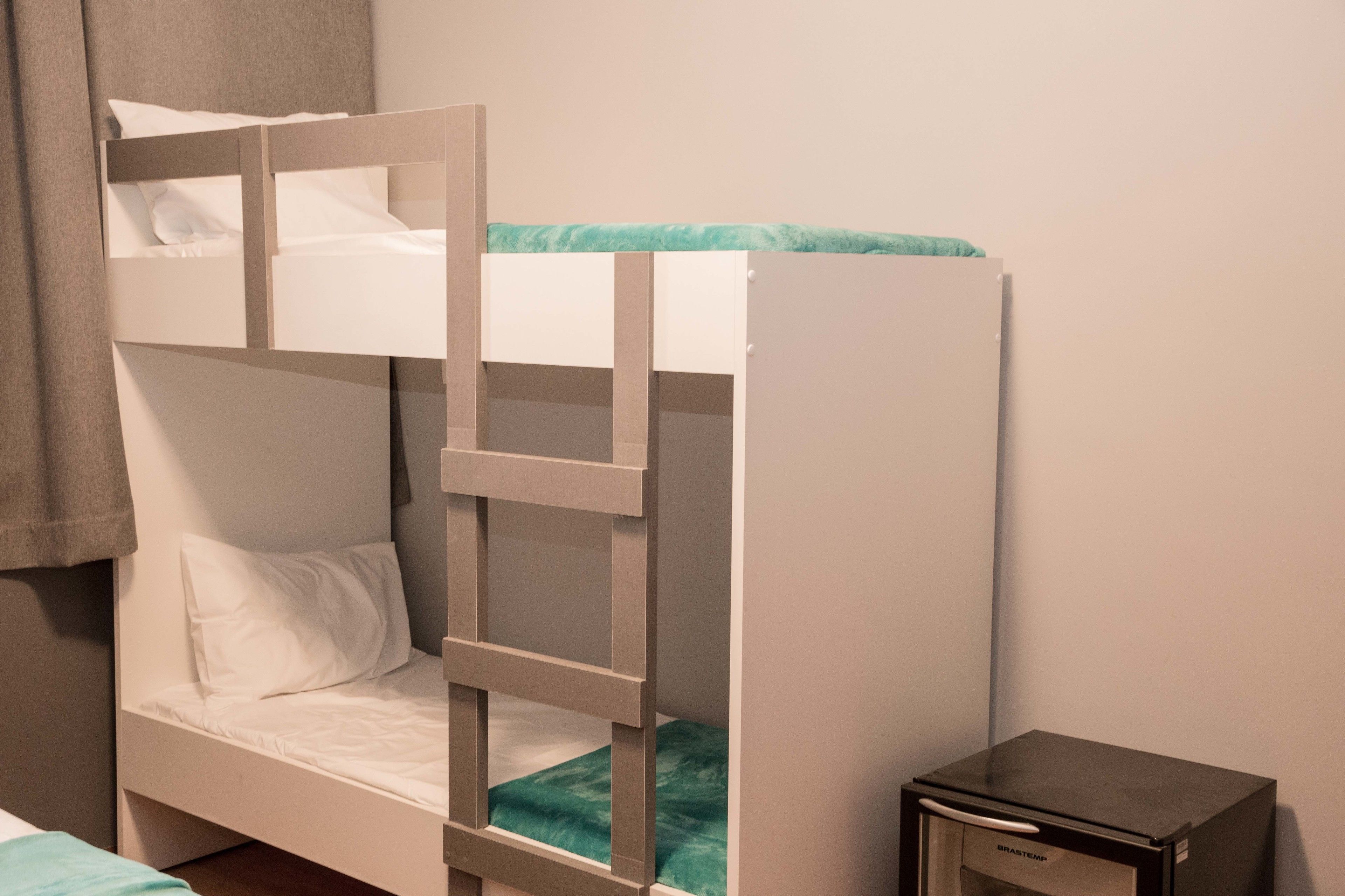 Un lit superposé avec une échelle, une petite table de chevet et un radiateur fixé au mur.