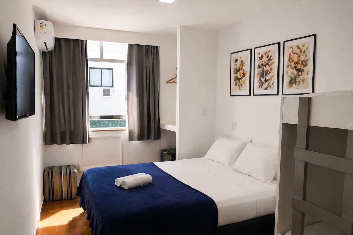 Une chambre d’hôtel avec un lit, une télévision, une fenêtre avec des rideaux et trois tableaux encadrés accrochés au mur.