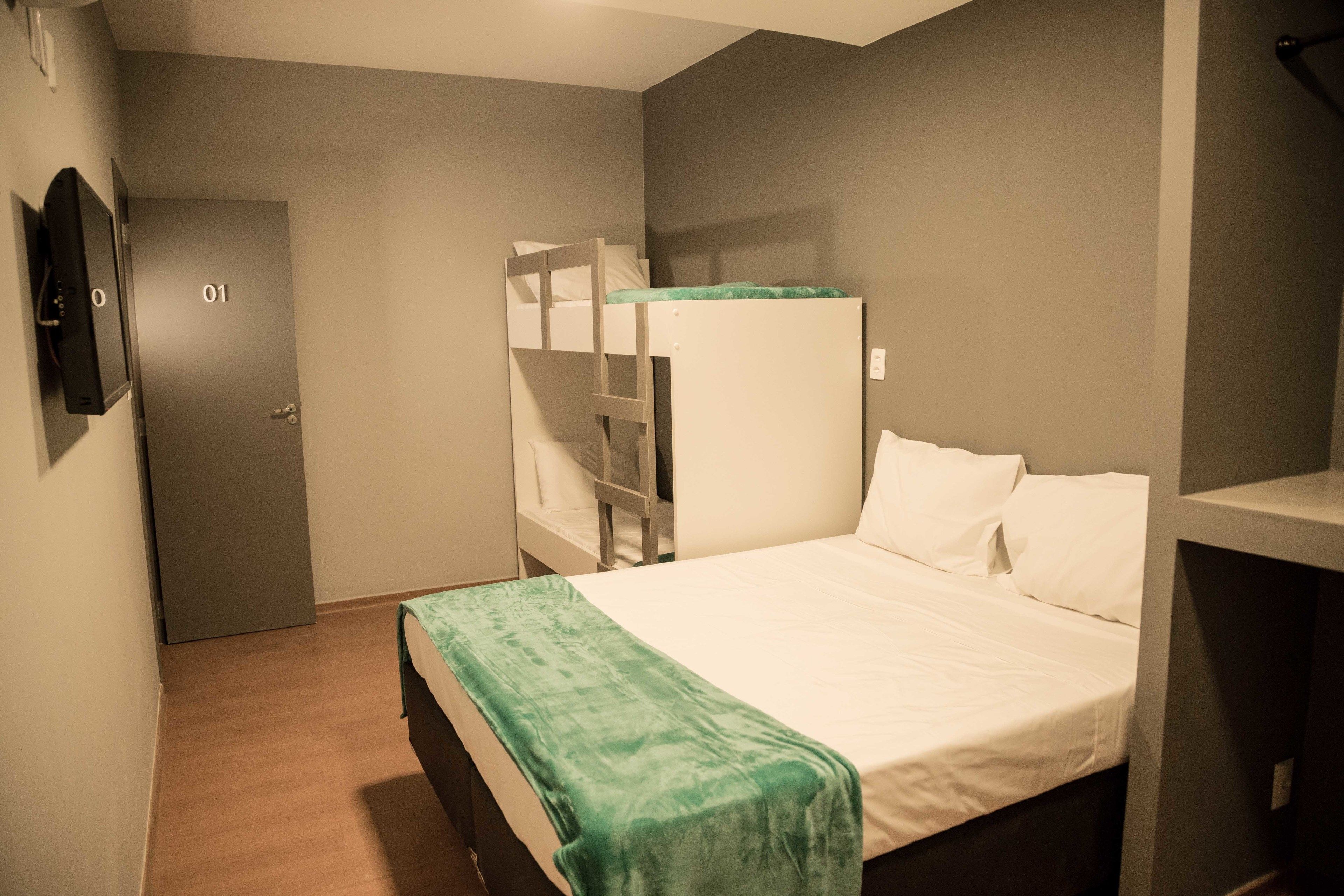 Una habitación con una litera, una cama individual, una puerta con un número y un televisor en la pared.
