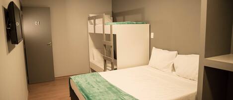Una habitación con una litera, una cama individual, una puerta con un número y un televisor en la pared.