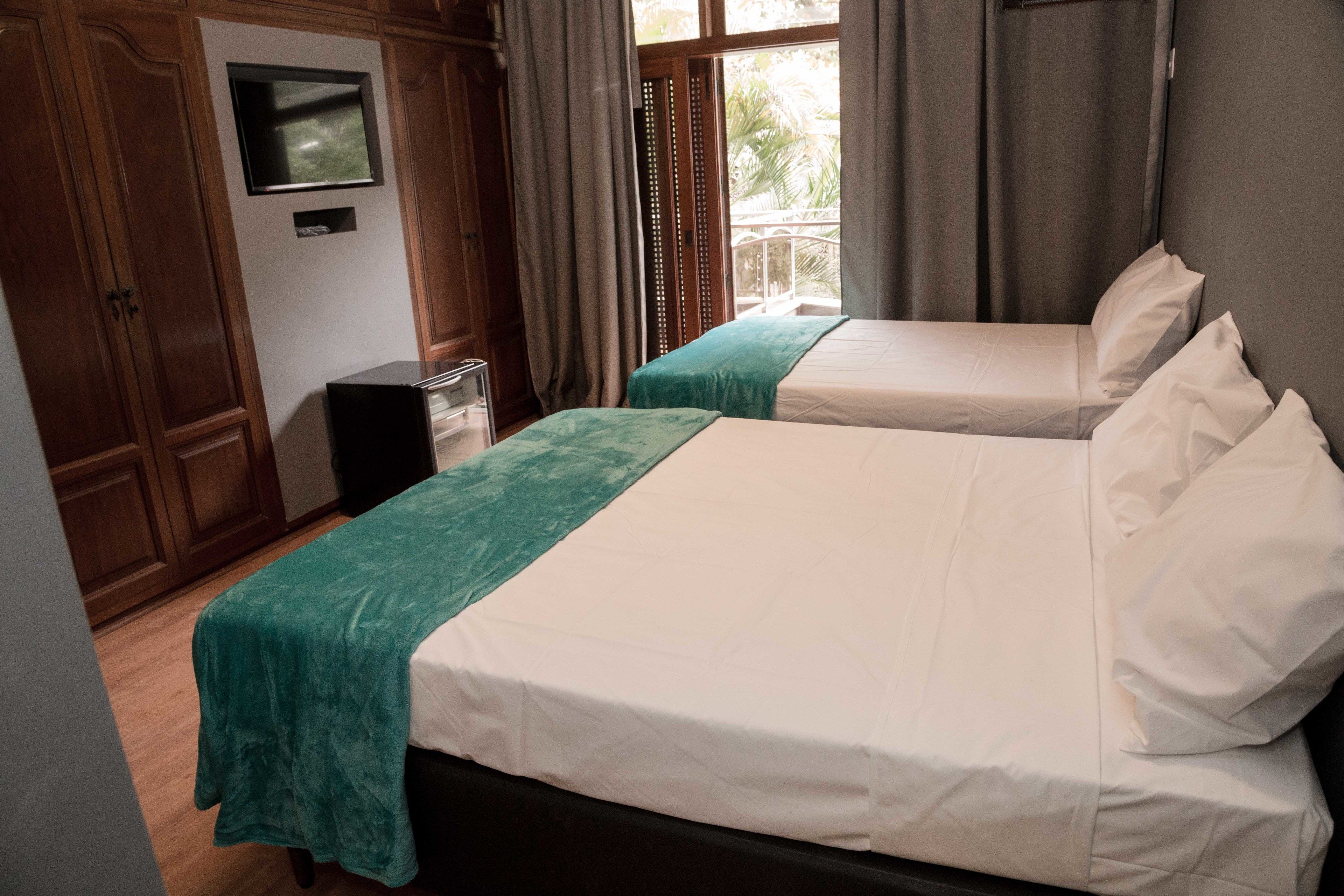 A hotel room with two beds, a TV, wooden wardrobe, and a balcony with curtains.