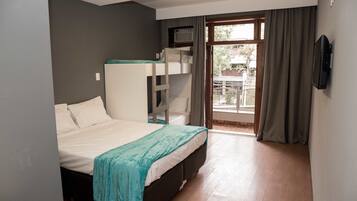 Un dormitorio con una cama litera, un televisor de pantalla plana montado en la pared y un ventanal corredero que da a un balcón.