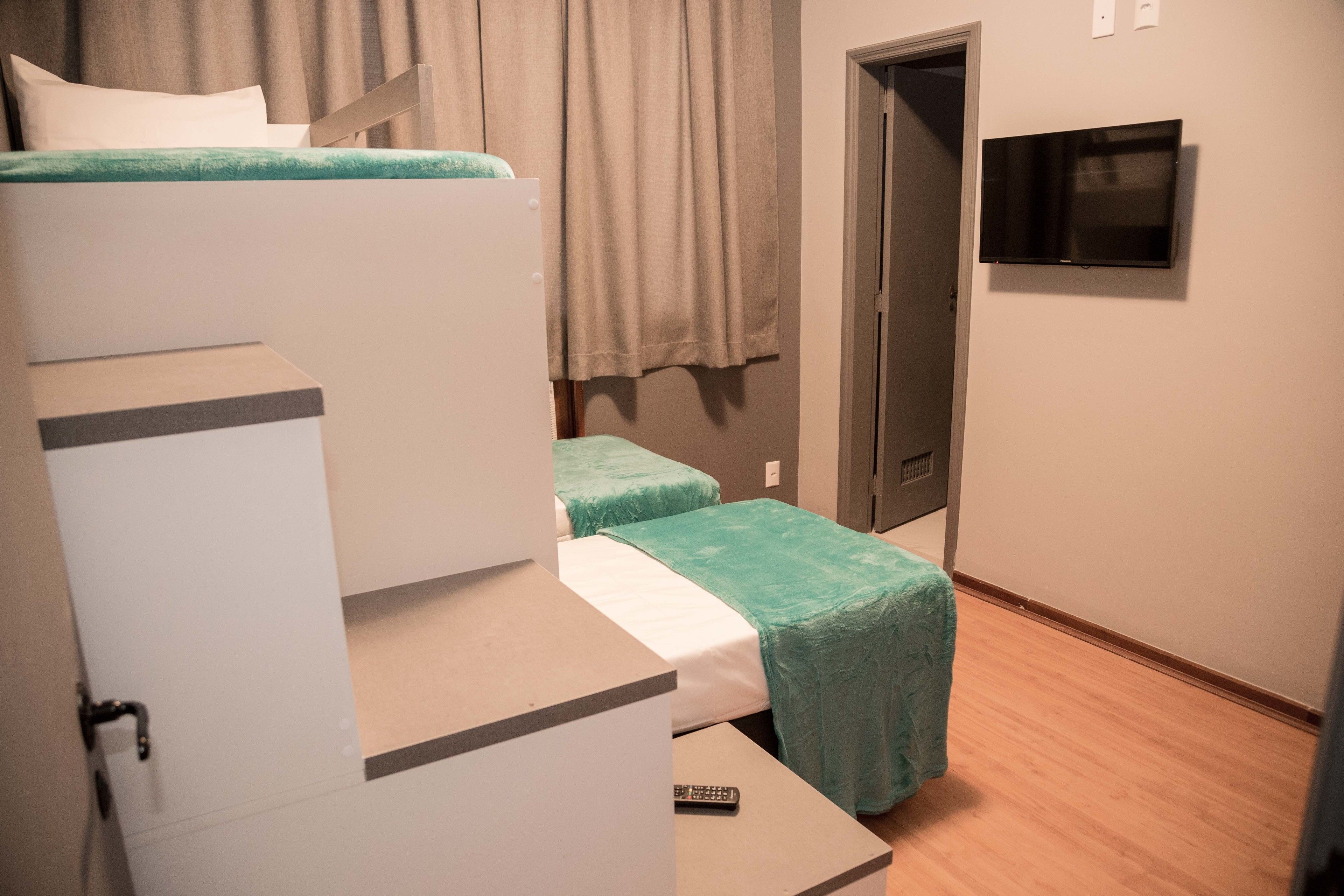 Una habitación con una cama litera, un televisor de pantalla plana montado en la pared y una puerta que da a otra habitación.