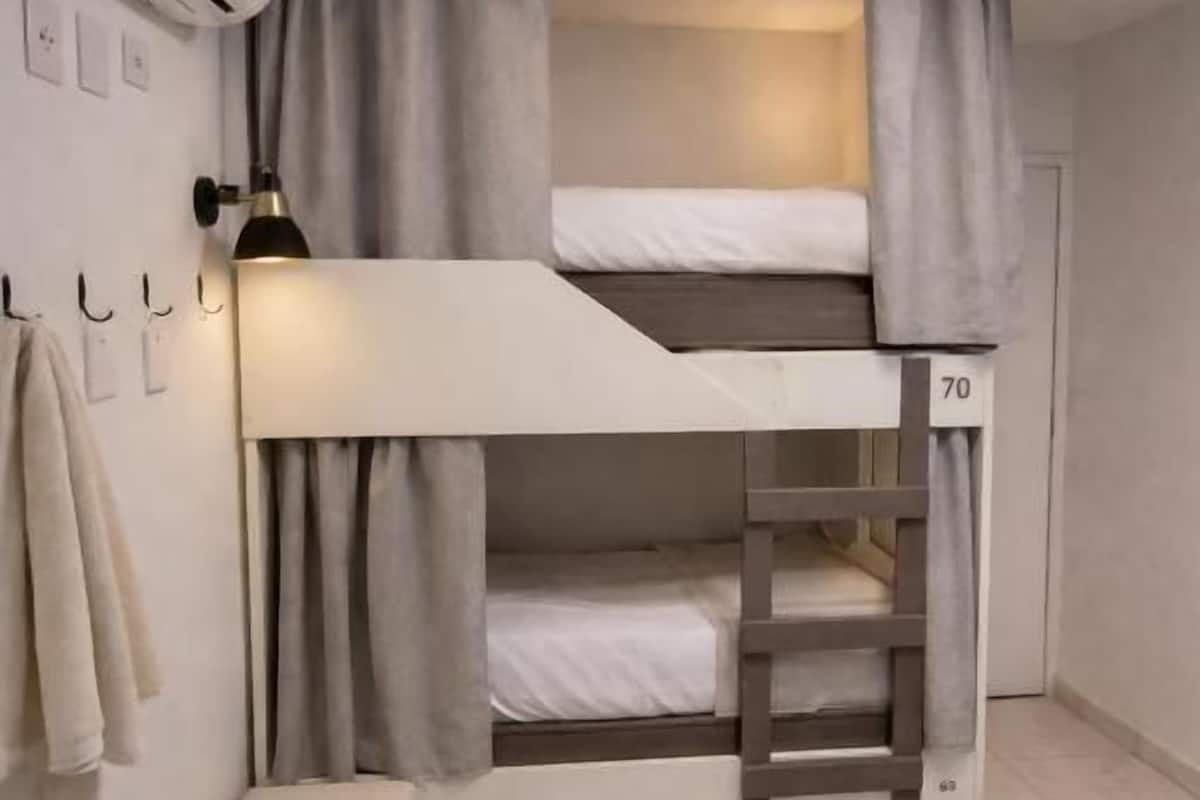 Un lit superposé avec le numéro « 70 » peint sur le côté, une petite table de chevet et un appareil de climatisation fixé au mur.