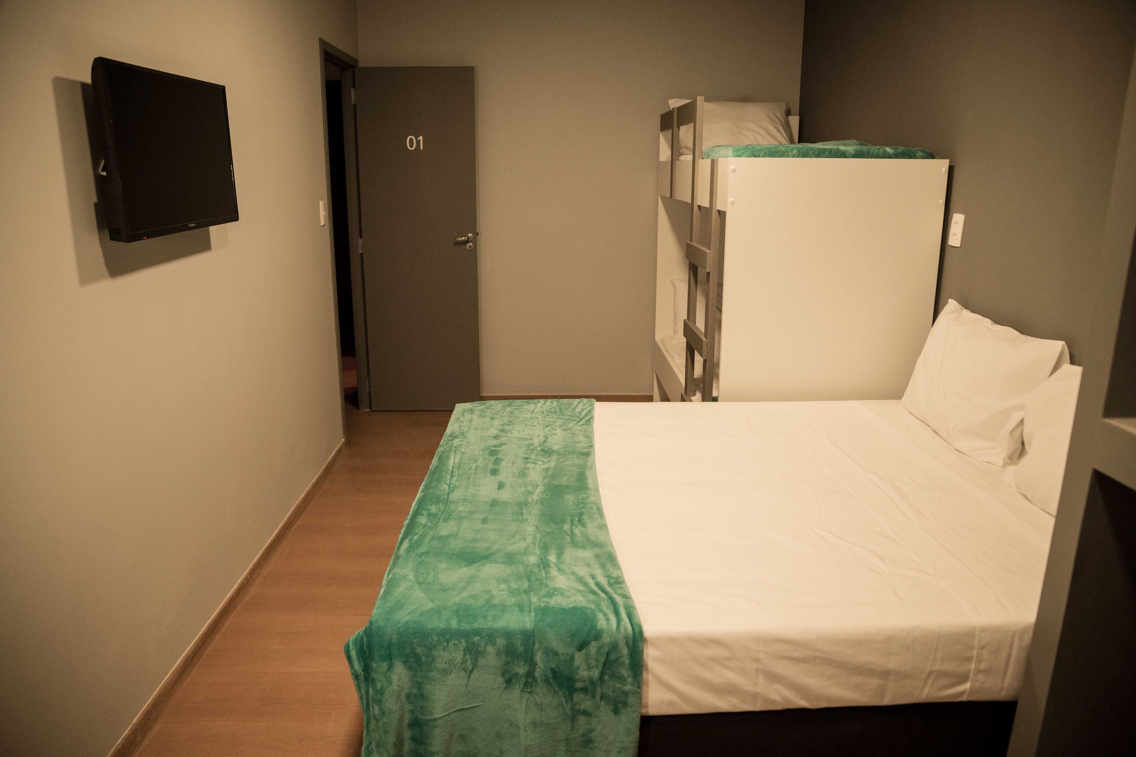 Une chambre avec un lit superposé, un lit simple, une couvre-lit verte, un téléviseur à écran plat fixé au mur et une porte portant le numéro 01.