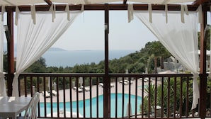 A balcony with a view of a swimming pool and a beach. - Naftilos (Samos)