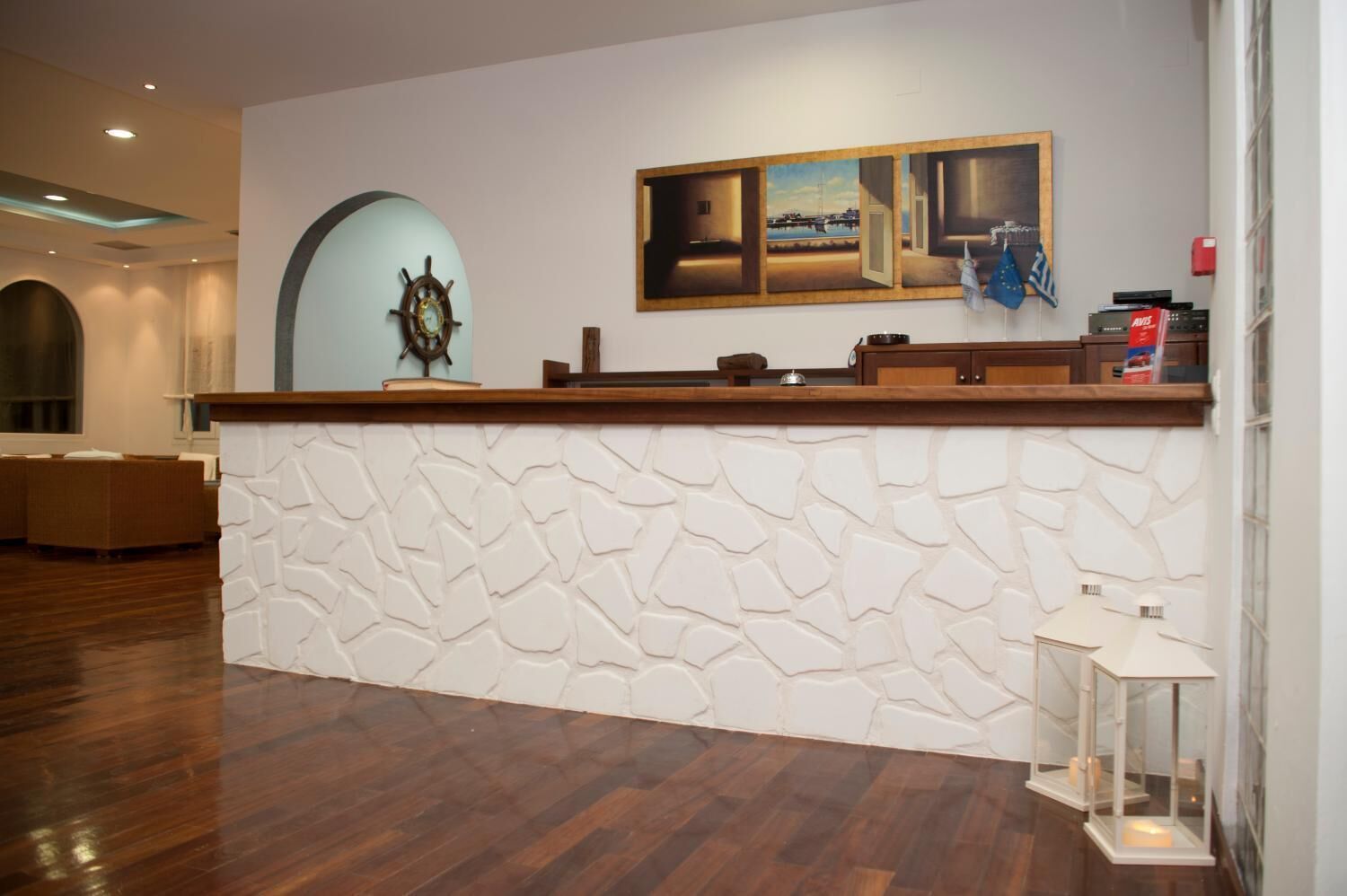 A reception area with a stone-textured wall, a wooden reception desk, a ship's wheel decoration, and a painting of a harbor scene.
