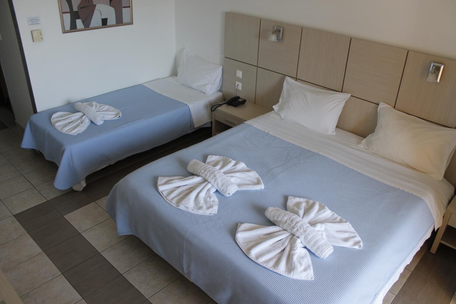 Une chambre d’hôtel avec deux lits, chacun recouvert d’une couvre-lit bleue et agrémenté d’oreillers blancs. Des serviettes sont disposées en forme de nœud sur les lits.