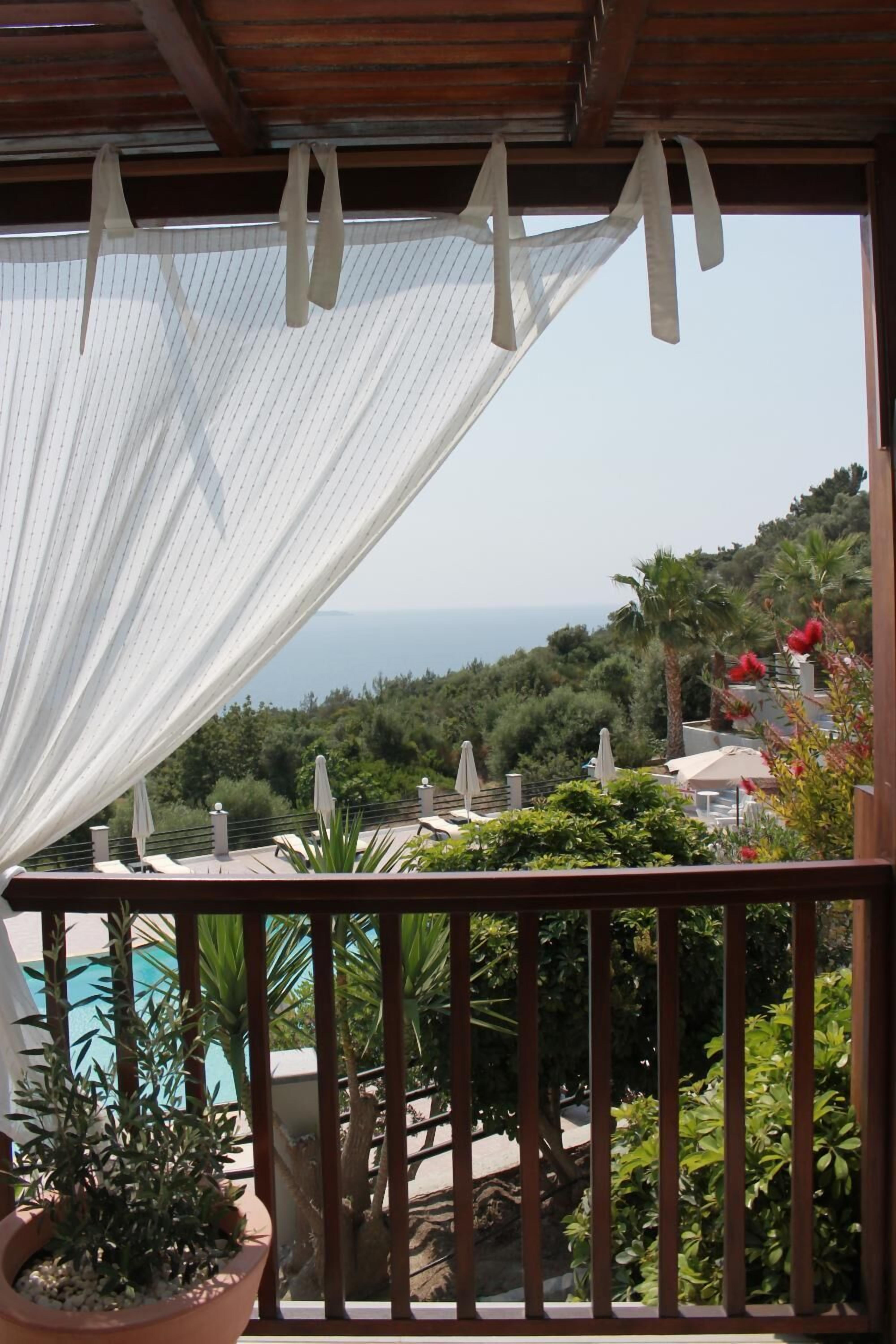A balcony with a view of the sea, potted plants, and outdoor furniture.