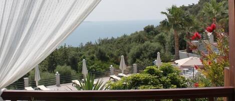A balcony with a view of the sea, potted plants, and outdoor furniture.