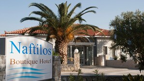A sign for Naftilos Boutique Hotel with a stone wall and palm trees in the foreground. - Naftilos (Samos)