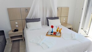 A hotel room with a large bed, two bedside tables, a nightstand, a tray with breakfast items, and a canopy bed. - Naftilos (Samos)