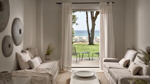 A minimalist living room with a sofa set, a coffee table, and a view of a beach and palm trees through a large window. - The Bay (Zakynthos)