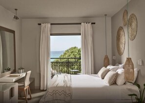 A bedroom with a bed, a desk, a chair, a balcony with a view of the sea, and decorative wall art. - The Bay (Zakynthos)