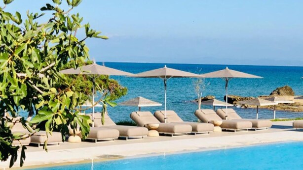 A poolside area with lounge chairs and umbrellas, overlooking a body of water. - The Bay (Zakynthos)