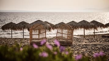 A beach with thatched umbrellas and wicker birdcages.