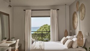A bedroom with a bed, a desk, a chair, a balcony with a view of the sea, and decorative wall art. - The Bay (Zakynthos)