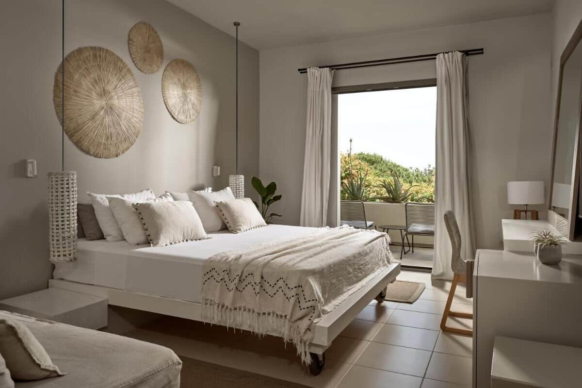 A bedroom with a bed, a desk, a chair, and a view of the outdoors.