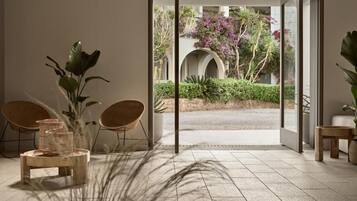 An interior space with a view of an outdoor garden through a glass door, a seating area with chairs, and a table with a plant.