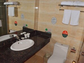 Un baño con lavamanos, espejo e inodoro. Hay toallas colgadas en un perchero y un cubo de basura.