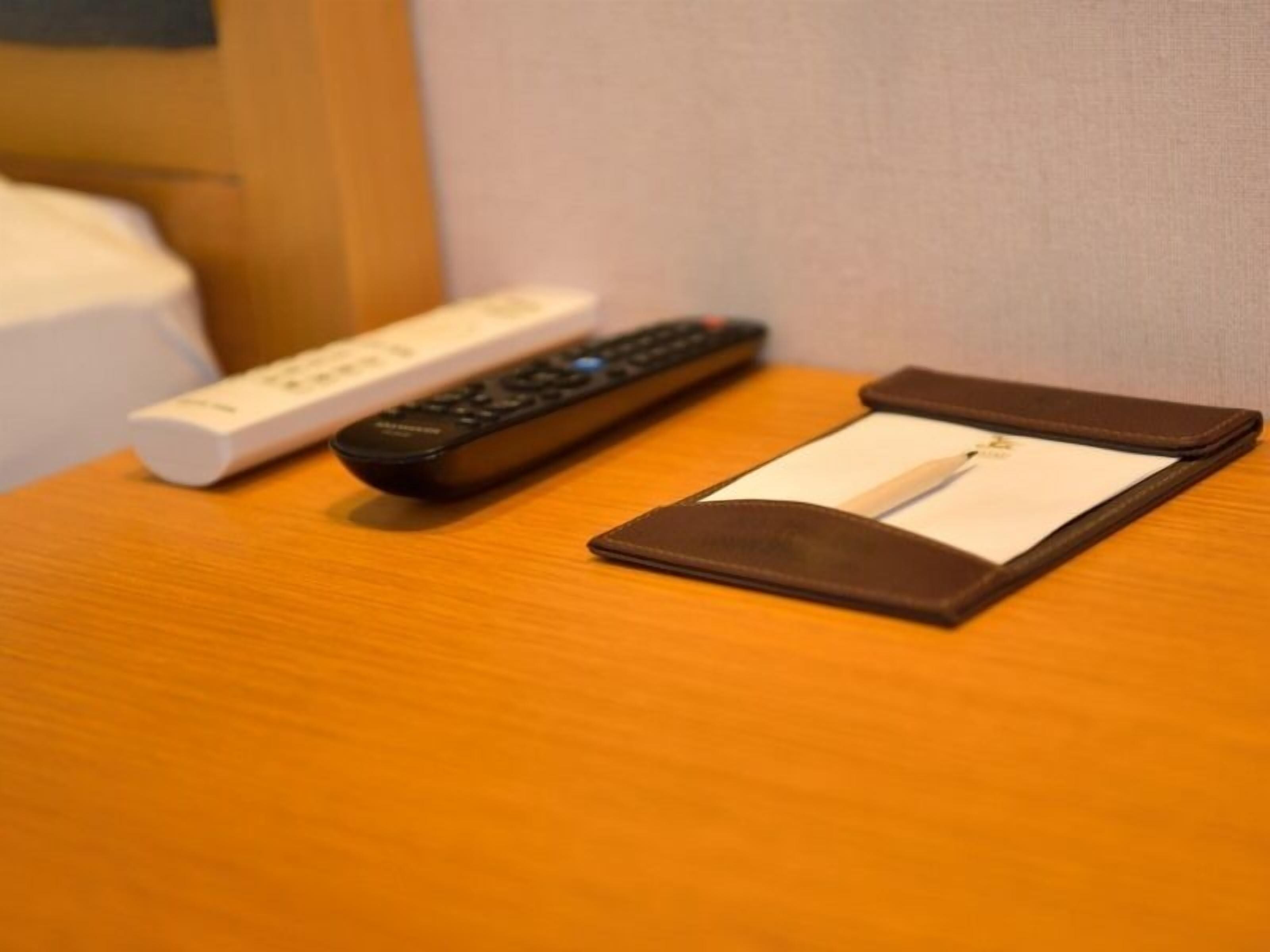 A remote control and a pen in a brown case on a wooden surface.