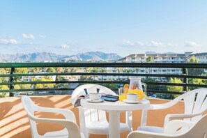 A balcony with a table set for breakfast, including a pitcher of orange juice and a cup of coffee, overlooking a residential area with mountains in the distance. - Aparthotel Alcudia Beach (Alcúdia)