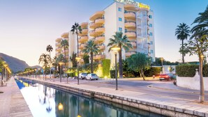 A hotel with multiple balconies, a pool, and a street with parked cars. - Aparthotel Alcudia Beach (Alcúdia)