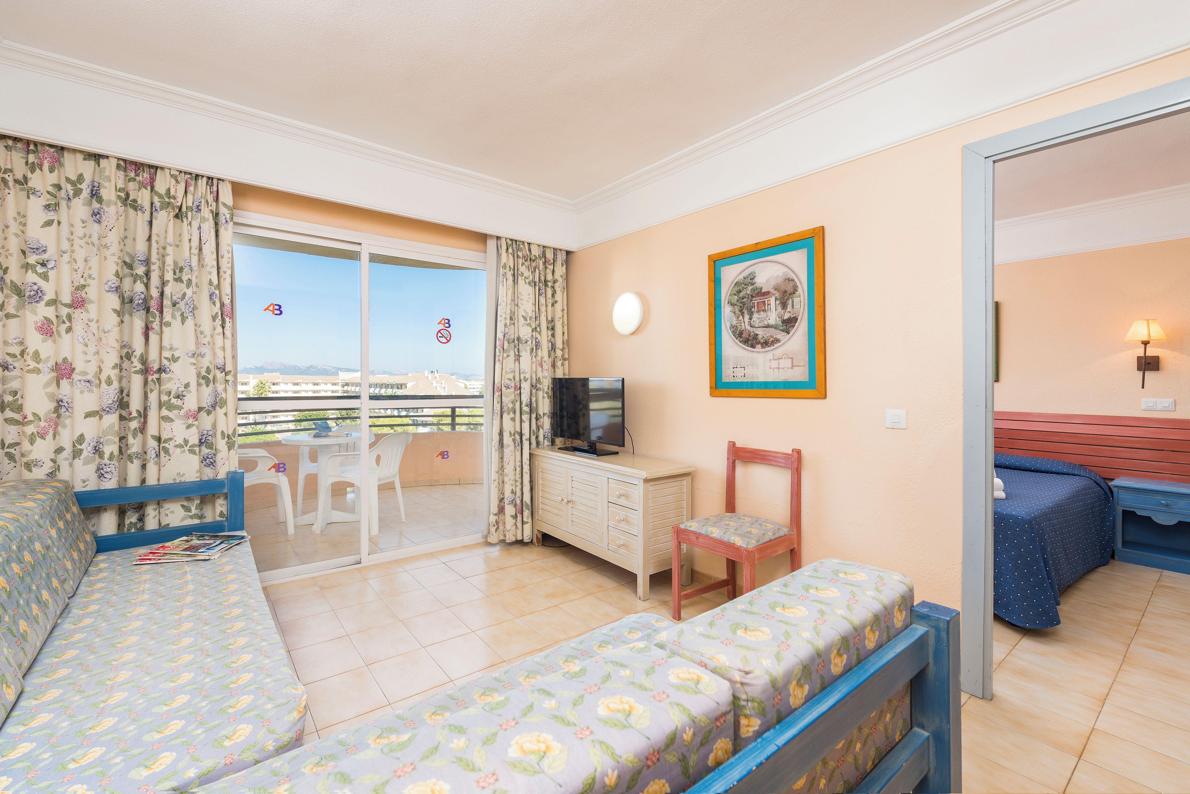 Quarto de hotel com varanda, televisão, cama, poltrona e escrivaninha.