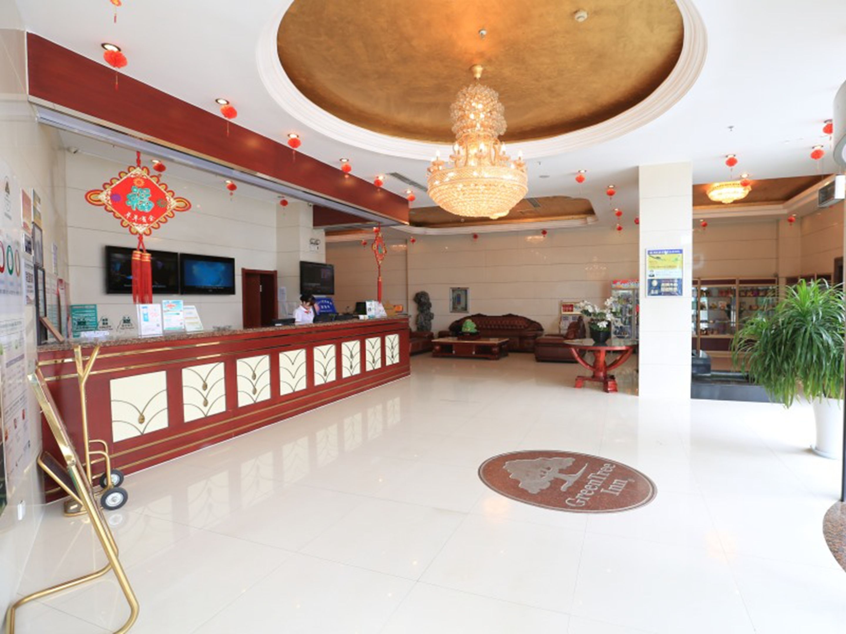 A hotel lobby with a reception desk, a chandelier, a sofa, and a potted plant.