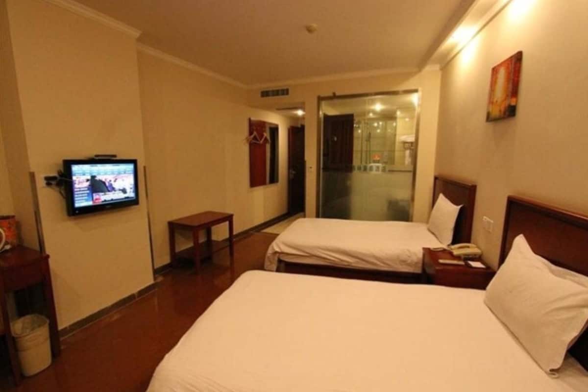Ett hotellrum med två sängar, en tv på väggen, ett litet bord och en papperskorg.