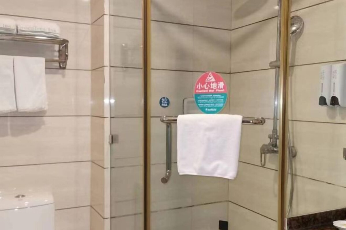 Un baño con cabina de ducha de vidrio, un perchero con una toalla blanca y un cartel que indica ducha con baja presión.