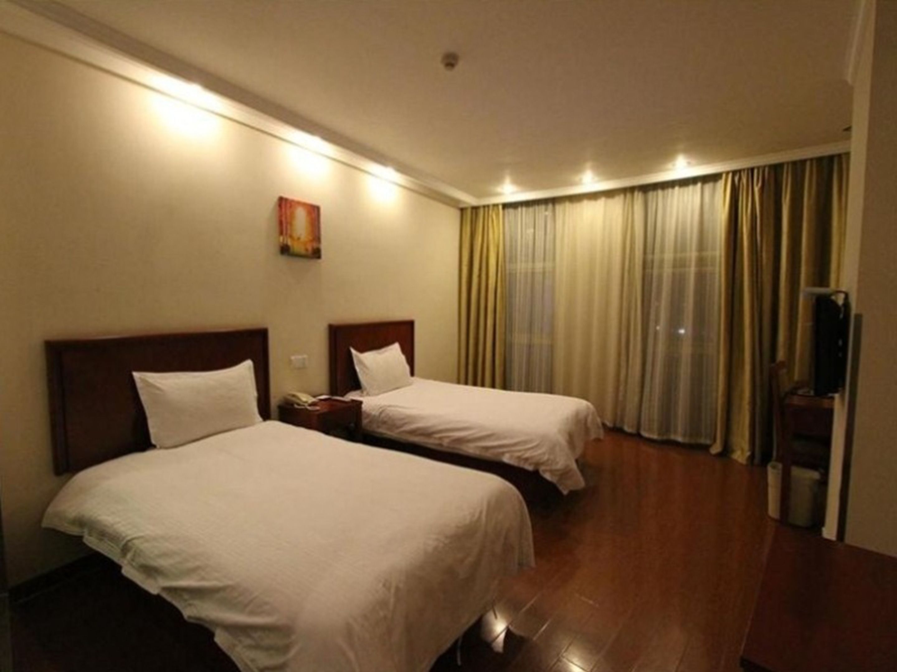 A hotel room with two beds, a painting on the wall, and a large window with curtains.