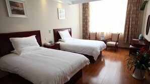 A hotel room with two beds, a desk, a chair, a potted plant, and a window with curtains. - GreenTree Inn Nantong Tongzhou District Pingchao Bus Station Express Hotel (Nantong)