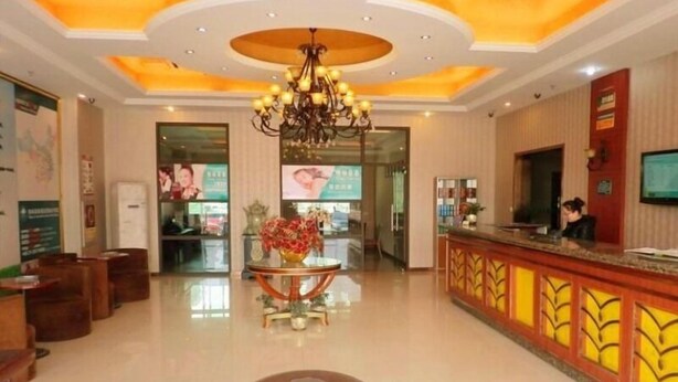 A hotel lobby with a reception desk, a chandelier, a round table with a vase, and a logo on the floor. - GreenTree Inn Nantong Tongzhou District Pingchao Bus Station Express Hotel (Nantong)