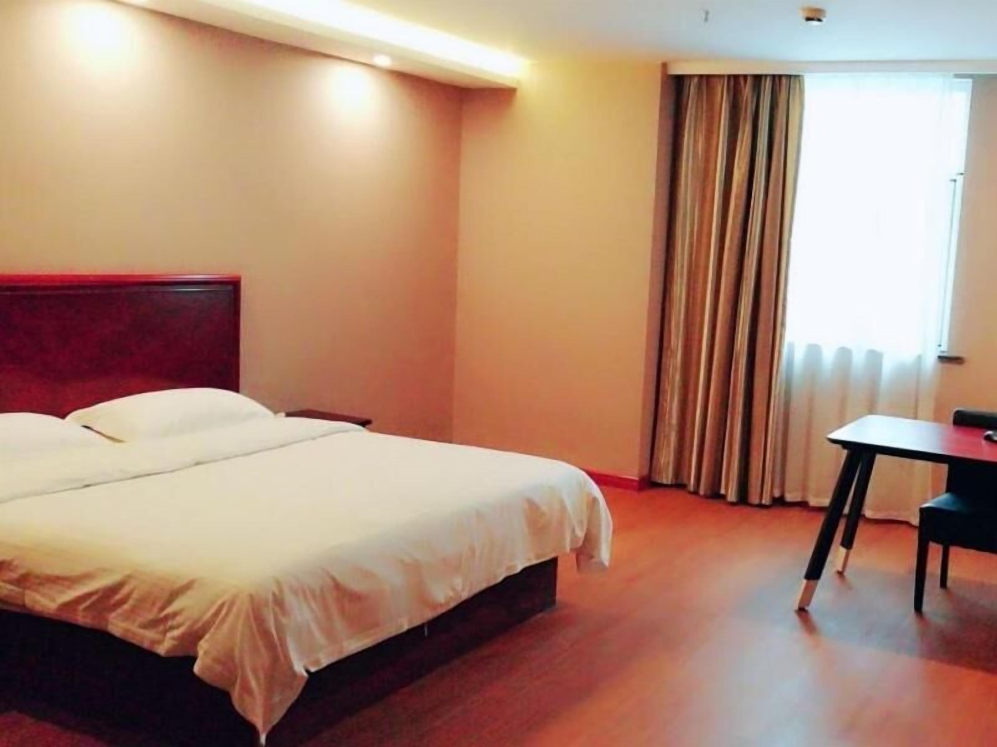 A hotel room with a large bed, a wooden headboard, a small table, and a chair.