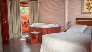 A bedroom with a bed, a wooden bench, and a hot tub. - Pousada Mares Do Santinho (Florianópolis)