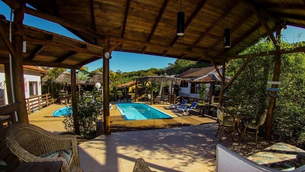 A covered outdoor area with a pool, lounge chairs, and a wooden deck. - Pousada Mares Do Santinho (Florianópolis)