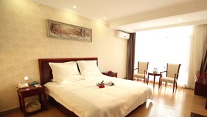 A hotel room with a large bed, a desk with a chair, a small table with a chair, and a painting on the wall. - GreenTree Business Inn HuiZhou South Railway Station DanShui RenMin Road Business Hotel (Huizhou)
