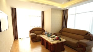 A living room with a sofa, armchair, and coffee table, wooden flooring, and large windows with curtains. - GreenTree Business Inn HuiZhou South Railway Station DanShui RenMin Road Business Hotel (Huizhou)