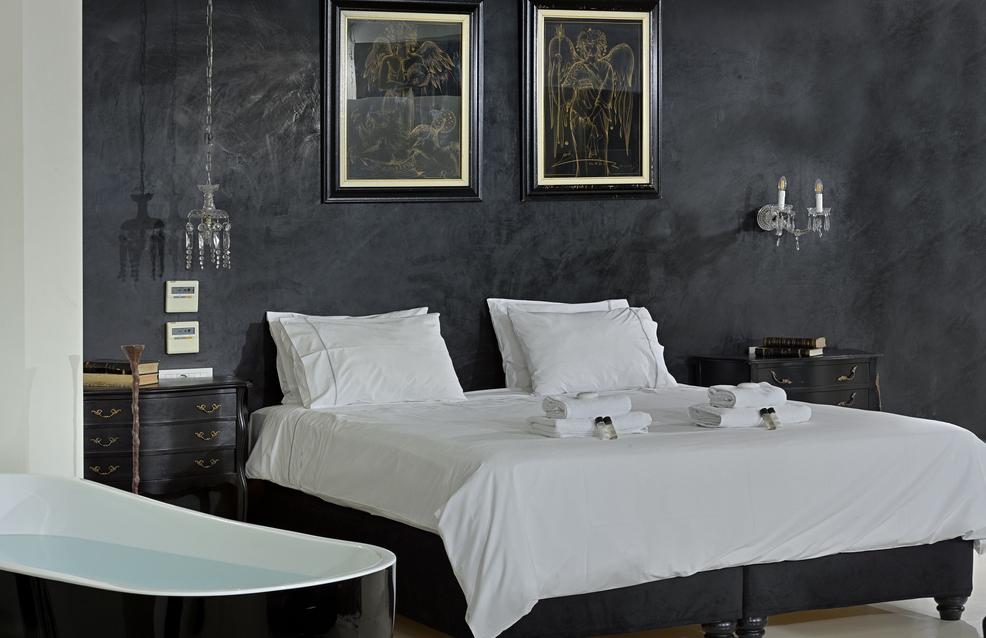 A modern bedroom with a large bed, a bedside table, a desk, and two framed artworks on the wall.
