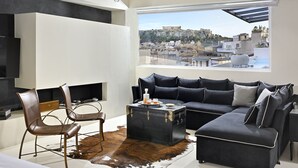 A modern living room with a large window, leather chairs, a black sofa, and a leather-bound coffee table. - Alto Psyrri Penthouse by K&K (Athens)