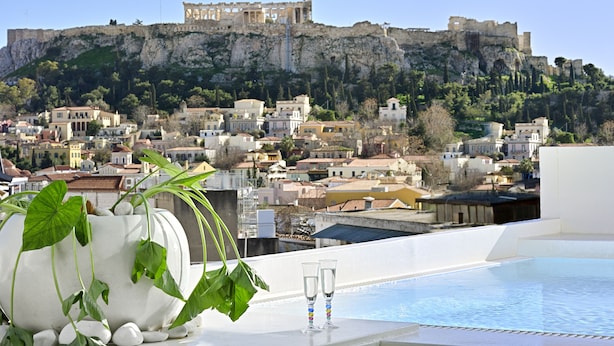 A rooftop pool with two glasses, a large vase with plants, and a view of a historic castle on a cliff. - Alto Psyrri Penthouse by K&K (Athens)