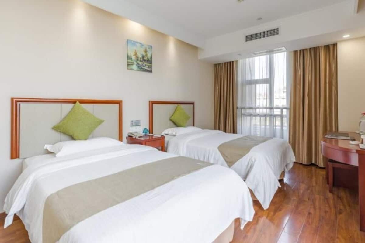 A hotel room with two beds, a desk, a chair, a window with curtains, and a painting on the wall.