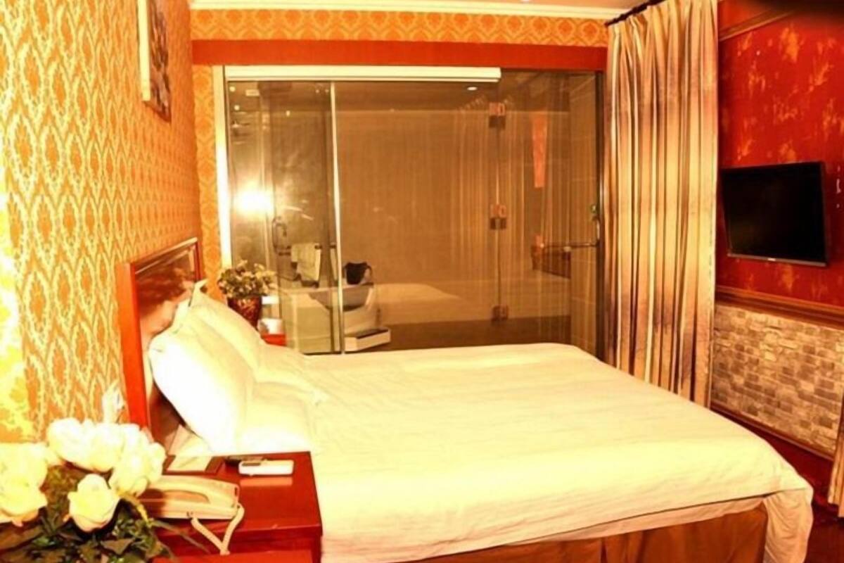 Une chambre d’hôtel avec un grand lit, un téléviseur fixé au mur et une porte-fenêtre coulissante donnant sur un balcon.