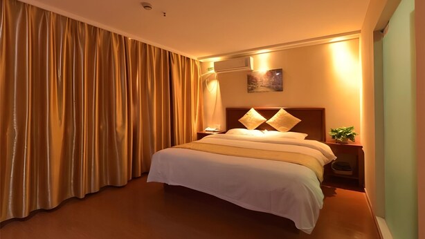 Een hotelkamer met een bed, gordijnen, een nachtkastje en een wandlamp.
